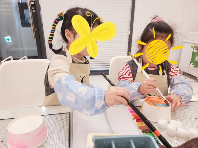얼굴 가림이 있는 두 아동이 붓과 물감으로 작업하는 모습