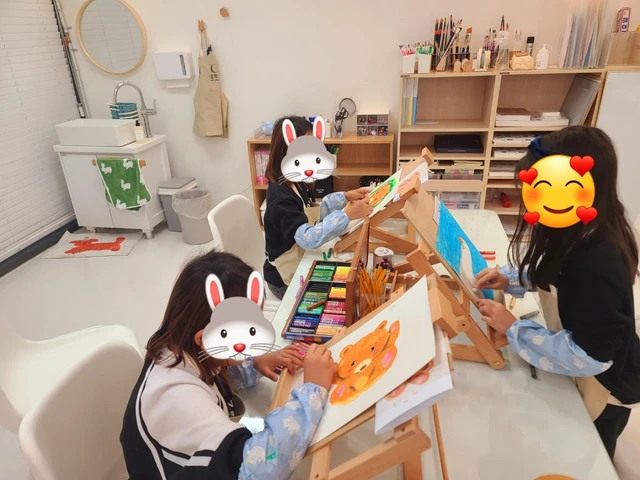 얼굴 가림이 있는 아동들이 나무 이젤에서 그림을 작업하는 모습